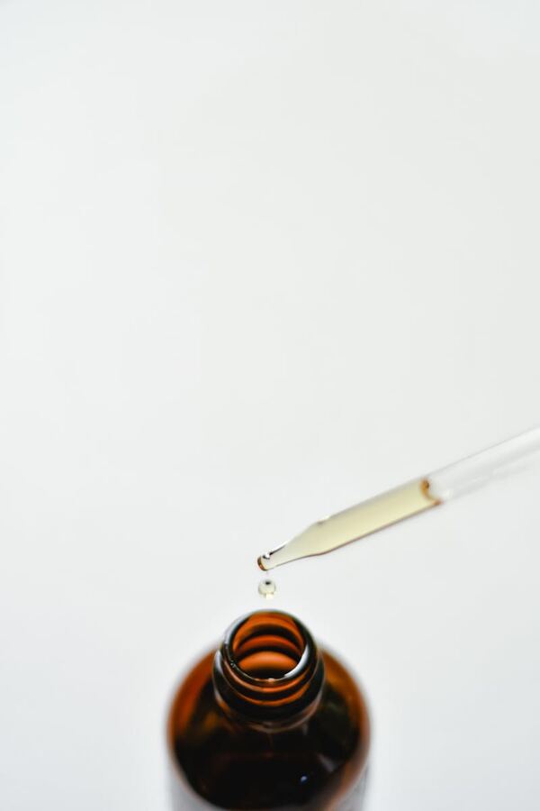Essential oil dropper releasing a drop of pure oil into an amber glass bottle